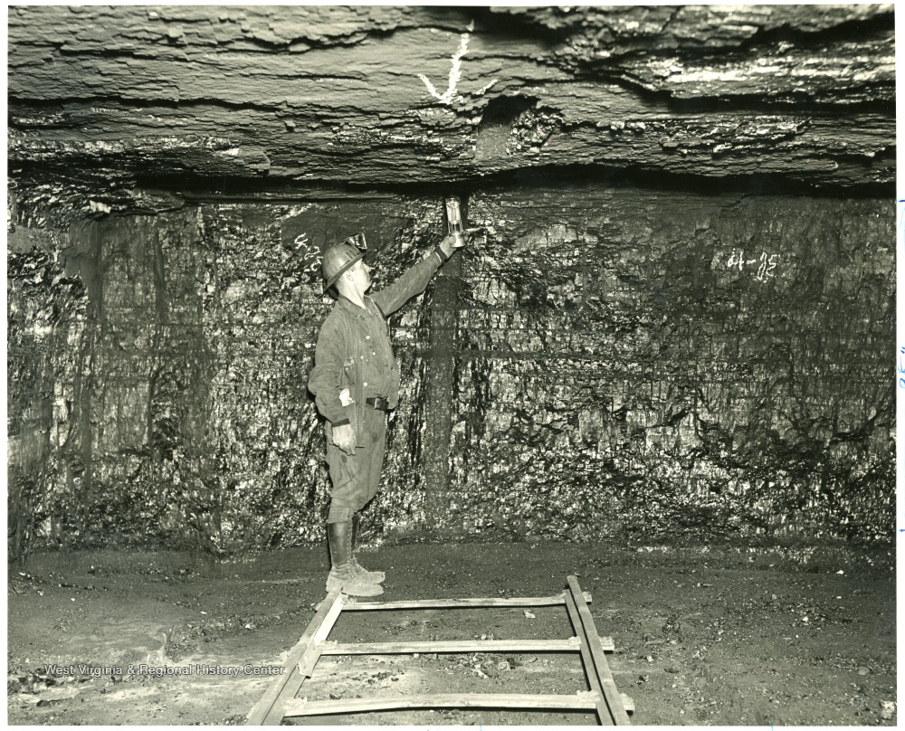 A man stands in the mining shaft holding an instrument to test the gas levels in the mine.