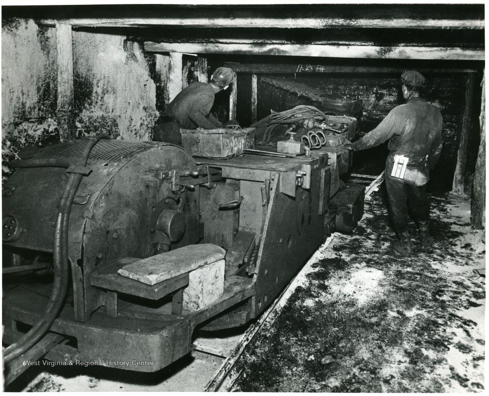 Two miners operate a track mounted coal cutting machine.
