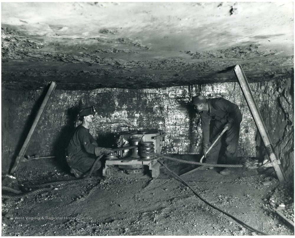 Two miners work with a machine to undercut coal.