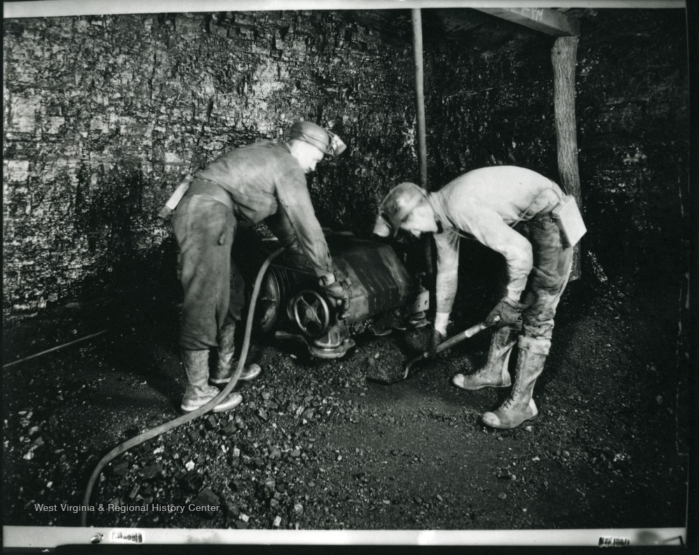 A miner is shoveling coal while another miner is operating a machine at an unidentified coal mine near Grafton, West Virginia.