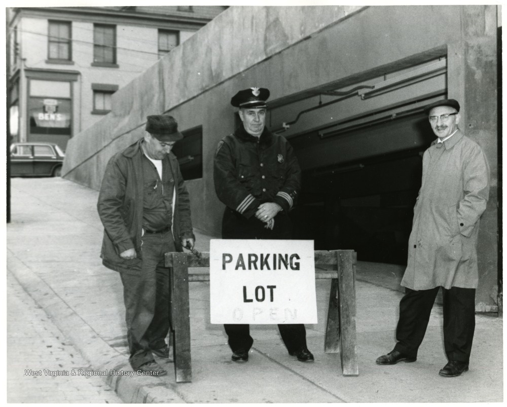 View of Parking garage entrance on Pleasant St. with workman (left to right) Harry Franks, Chief John Lewis, and Milton Cohen standing behind a sign.
