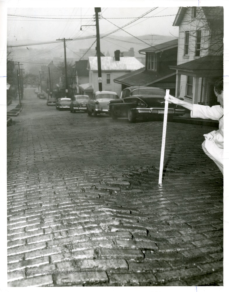 A man is measuring depth of street brick subsidence on North Spruce Street in Morgantown, West Virginia.