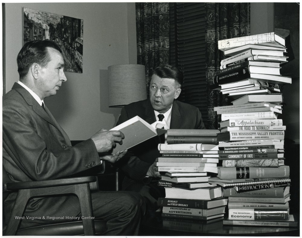 'John Luchok, University editor, (at left) looks over books written by the professors honored at May 11 Authors' Banquet with Dr. Harry B. Heflin, acting WVU President.' 