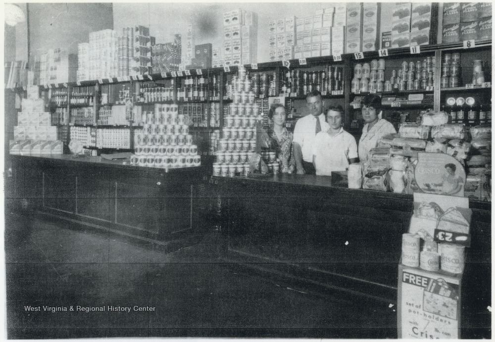 Inside the store located on the corner of 3rd Avenue, between Ballengee and Temple streets. Employees behind the counter are identified, from left to right, as Lorene Jones, an unidentified man, Mary Eades, and Maycle Scott who is the mother of Jack Scott. 