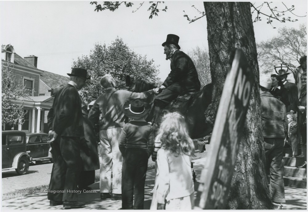 Moorman Parker sits on top of a horse to perform the re-enactment in front of the First Methodist church building located on the corner of Ballengee Street and Third Avenue. Other subjects and spectators unidentified. 