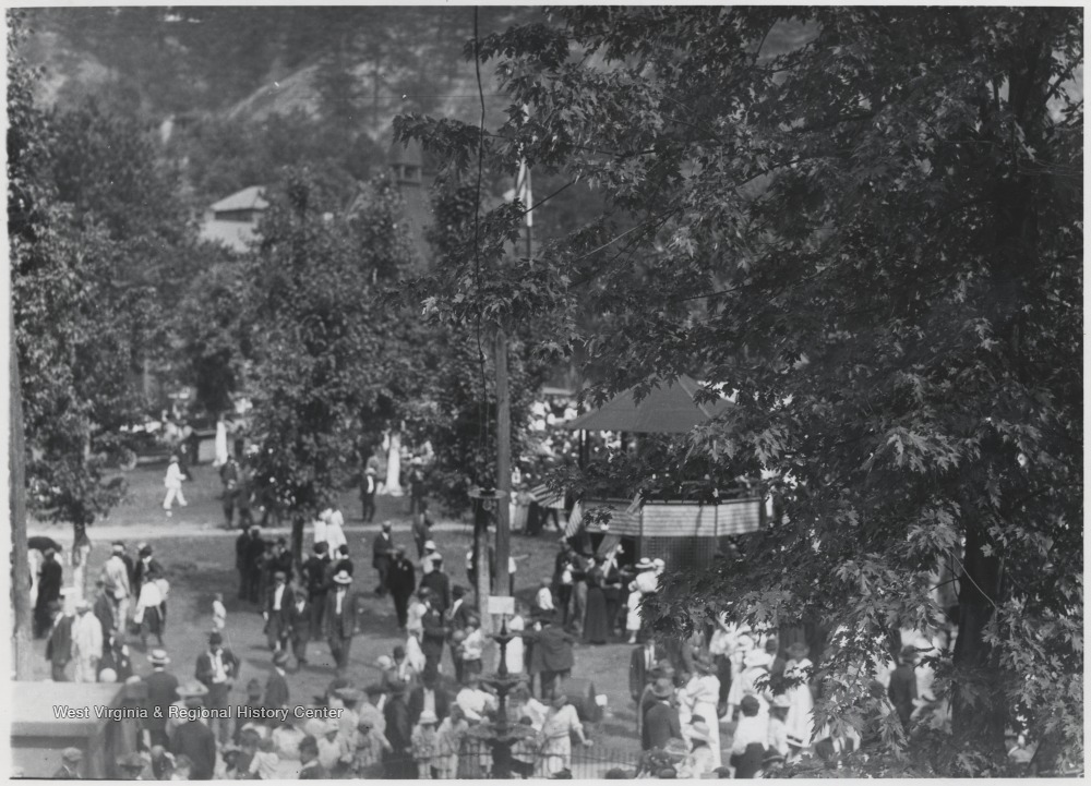 A crowd gathers across the lawn and around a pavilion decorated with American flags.