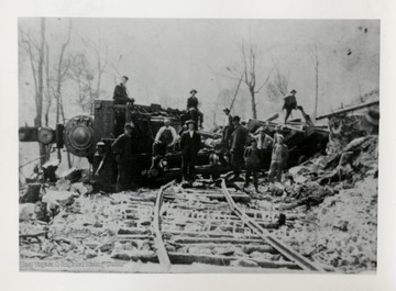 Men standing in front and on top of train wreckage.  