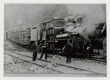 Train engine with log carts.  Two men in engine, four men standing by tracks.  