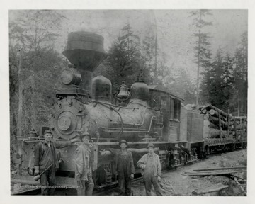 Train engine with log carts and four of its crew members standing in front of it.  (Left Side 3/4 Front) Charles Cramer and Alt Cramer.