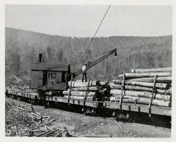 Loader putting lumber on cargo cars.  Man standing on logs on the car.  