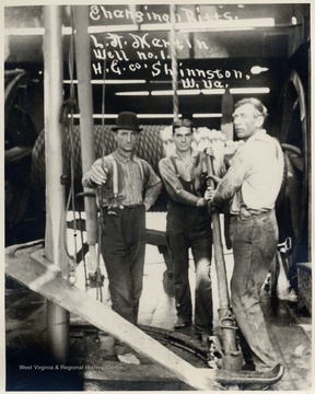Three men changing bits on an oil well drilling rig.