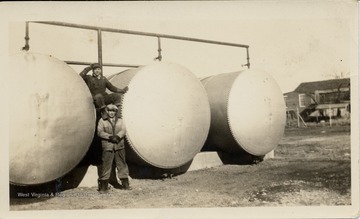 Two Men Standing in between three oil storage containers.