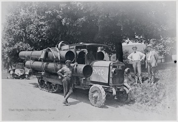 Men standing beside a halftrack carrying oil equipment.