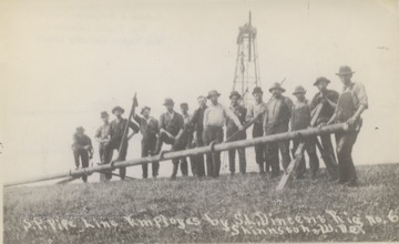 Group portrait of oil workers standing behind pipe line.