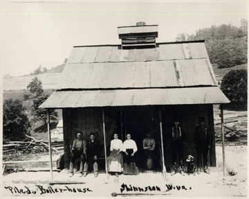 Group Portrait of five men, two women, and a dog on the porch of a Boiler House.