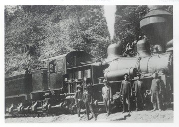 Train crew and other men stand in front of an engine.