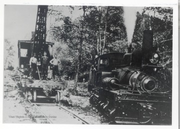 Train engine pulling part of a wrecked train.  Crew members standing on crane car.