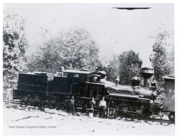Side view of a train engine and crew members standing in front of it.