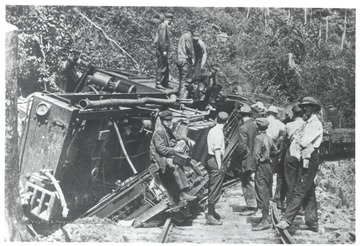 Group of men standing next to and on top of a wrecked train.