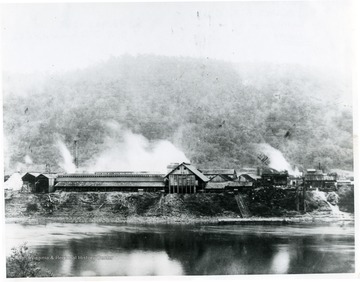 View of Dickinson Salt Works from opposite bank of Kanawha River. Made about 1910. This is the only picture in existance showing salt loaded on barge for ferrying across river where it was loaded on C&O Railroad. The New York Central Railroad had served the plant for years before this picture was taken, but due to higher freight rates by the NYC, it was still possible to ship by C&O to some points at a saving.
