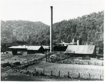 A smokestack in the center surrounded by salt works buildings.