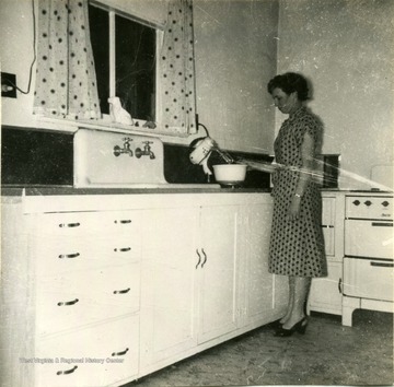 Photograph showing improvements of the kitchen of Mrs. Carl Maxwell of Harrison County.  'Took out full size window and put in a small one, built cabinets around sink. Planned to add wall cabinets.'