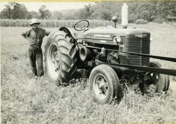 Man standing next to a tractor with a belt attached to it in Hancock County.