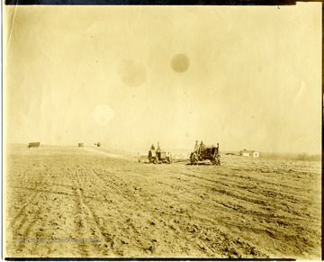 Men spreading lime with tractors on the fields at Arthurdale, getting ready for potatoes.  Small windmill visible in background.