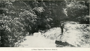 A man stands on a rock that juts out into the side of a stream.