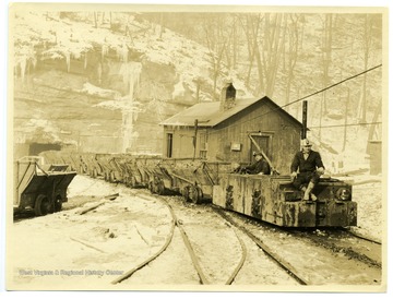 Two miners riding a electric locomotive outside of a mine during the winter. 