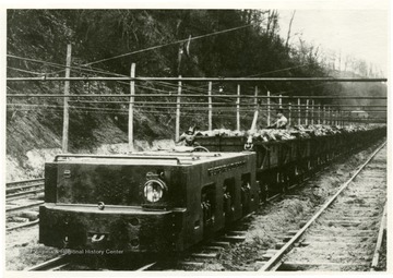 An electric locomotive carrying coal and miners outside of the mine. 