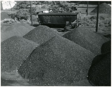 Piles of coal with a filled coal car in the background.