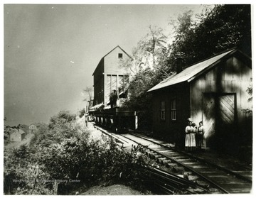 Men standing on top of coal cars with a woman and two children on the ground.