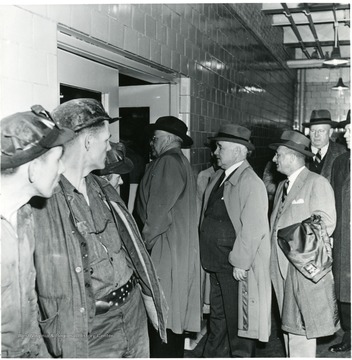 Three miners watch a line of coal officials entering a room during a Consolidation Coal Co. Inspection trip.