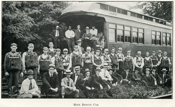 Group portrait of men, some in rescue attire, standing in front of the mine rescue car.
