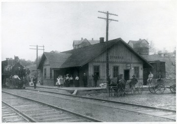 Group of people wait at the train station as a train comes in.  
