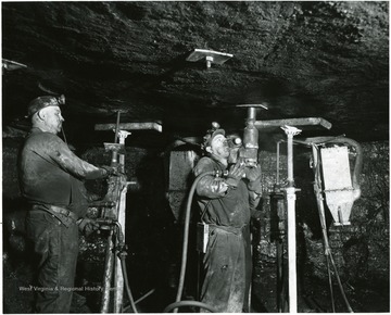 Three miners putting bolts in the roof at Bishop Mine. Jacks used to hold the roof up while this process was being done. 