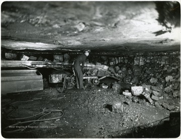 Miner standing over a mechanical loader at the Winifrede Seam, Sycamore Coal Co. Cinderella Mine, Mingo Co., W. Va.
