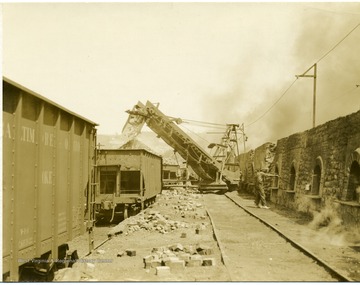 Miner works with coke ovens while a loading machine fills railroad cars.