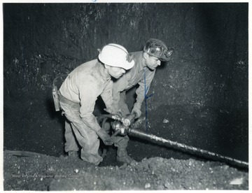 Two miners drill before placing charges.