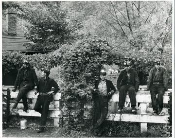 Miners take a break and sit on a fence.