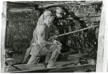 Two miners drill holes prior to placing charges. 'Holes are bored at proper intervals for shooting.'