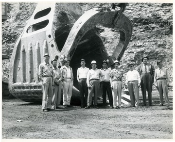 Group portrait of men standing next to large shovel scoop.