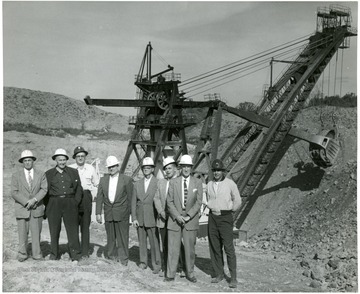 Group of men stand next to a large shovel.