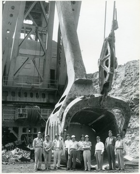 Group portrait of men standing in front of a giant shovel.