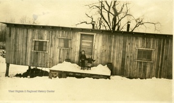 Children stand on porch in the snow outside of a barrack.