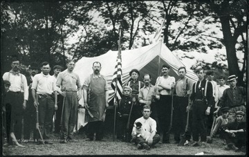 Group of men wearing badges and holding guns and an American flag stand near a tent.