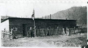 Man standing outside of barracks beside a flag at half mast.