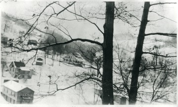 View through some trees of houses on snowy hillside in Farmington, W. Va.