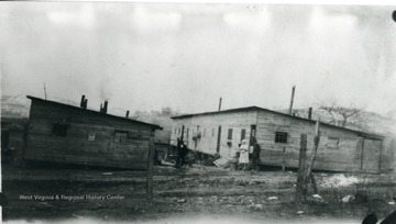 Two men and a woman standing near a barracks at Rivesville, W. Va.